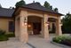 Beige house entrance with pillars and lanterns, surrounded by greenery and evening light.