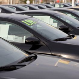 Row of black cars with sale signs on windshields, parked in a lot.