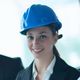 Woman in a blue hard hat smiling, wearing a business suit.