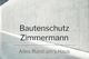 Text "Bautenschutz Zimmermann" auf Betonwand, Untertitel "Alles Rund um's Haus".