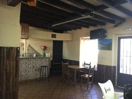 Interior rústico de un bar con mesas, sillas, barra y decoración de madera.