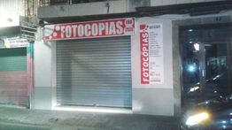 Fachada de una tienda de fotocopias cerrada de noche, con letrero rojo y blanco en la entrada.