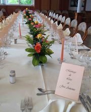 Langer, weiß gedeckter Tisch mit Blumenarrangement und eleganten Gedecken in einem Festsaal.