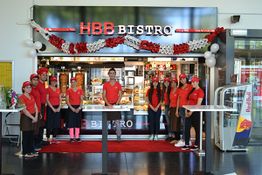 Gruppe von Menschen in roten Uniformen vor dem HBB Bistro, geschmückt mit roten und weißen Blumen.