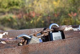Rusty chain with two locks securing a metallic surface, blurred greenery in the background.