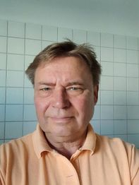 Eine Person lächelt leicht in die Kamera, im Hintergrund sind weiße Fliesen zu sehen.