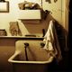 Old sink with faded towel and shelf clutter in dimly lit, rustic bathroom.