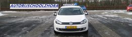 Witte Volkswagen lesauto op besneeuwde parkeerplaats met bord "Autorijschool Zhora".