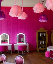 Salón de belleza infantil con paredes rosas, espejos iluminados y sillas color fucsia.