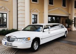 Weiße Limousine vor einem eleganten Gebäude mit Säulen und großen Fenstern geparkt.