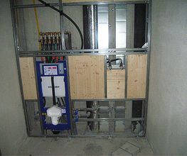 Freiliegende Sanitärinstallation in einem Rohbau mit sichtbaren Rohren und Leitungen.