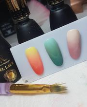 Muestra de uñas con esmalte en degradado de amarillo a rojo, verde y rosa. Botellas y pinceles atrás.