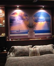 Dormitorio elegante con cama, mural de playa al atardecer, y estantes con adornos iluminados.