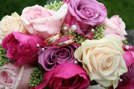 Rosenstrauß in Rosa- und Cremetönen mit goldenen Ringen verziert und Perlenfäden umwickelt.