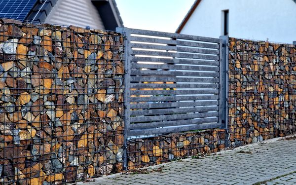 Eine Sichtschutz-Zaun aus Gabionen mit bunt befülltem Steinbruch. Als kreativen Zwischenelement wurde ein Metallzaun als Unterbrechung eingesetzt.