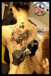 Person bekommt ein großes Tattoo eines Adlers mit Schriftzug auf dem Rücken von einem Tätowierer.
