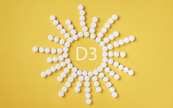 Weiße Tabletten sind auf gelbem Hintergrund in Form einer Sonne um die Aufschrift D3 angeordnet.