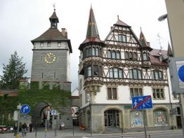 Historisches Stadttor und Fachwerkhaus mit einem Uhrturm in einer deutschen Stadt bei bewölktem Himmel.