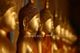 Reihe goldener Buddha-Statuen, schräg von der Seite fotografiert, mit warmem Licht beleuchtet.