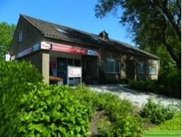 Bakstenen gebouw met rode borden, omgeven door groen, onder een blauwe hemel.