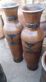 Due grandi vasi di ceramica marrone con decorazioni intricate su uno sfondo di altri vasi.