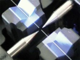 Nahaufnahme von zwei Mikroskopspitzen, die auf einen feinen Draht zeigen.