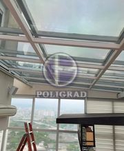 Vista de interior com teto de vidro e escada vermelha. Logo "POLIGRAD" sobreposto na imagem.