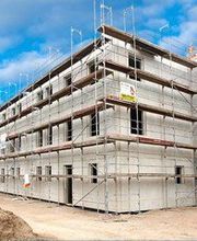 Ein mehrstöckiges Gebäude im Bau mit Gerüsten, klarer Himmel im Hintergrund.