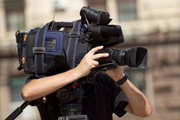 Person filmt mit großer Videokamera vor unscharfem Hintergrund.