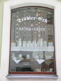 Schaufenster mit antikem Geschirr und Dekoration, Schriftzug "Trödler-Eck & Antiquitäten" oben.