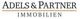 Logo von "Adels & Partner Immobilien" mit schwarzer Schrift und goldener Linie.