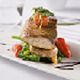 Gourmet dish with meat, greens, and cherry tomatoes on a white plate, elegantly garnished.