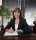 Smiling woman in office with plants, writing on paper at desk.