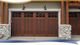 Wooden garage door with glass panels, stone pillars, and outdoor lights mounted above it.