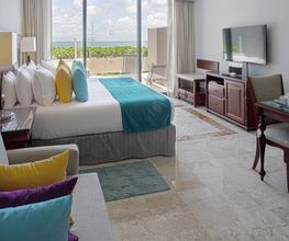 Habitación luminosa con cama, almohadas de colores y vista al mar desde el balcón.