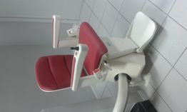 Sedia motorizzata per scale con rivestimento rosso, su binario curvo, in un ambiente chiuso.