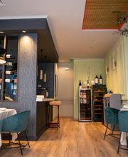 Restaurante elegante con mesas blancas y sillas turquesa, estantes de vino y decoración moderna.