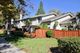 Two-story house with wooden fence, lush greenery, and a clear blue sky.