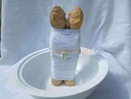 Deux figurines en bois, enroulées ensemble de fil blanc, sont placées dans un bol blanc.