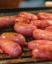 Linguicinhas grelhadas em uma churrasqueira, com aparência suculenta e dourada.