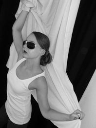 Frau in weißem Top und Sonnenbrille hält eine weiße Decke, im Schwarz-Weiß-Foto posierend.