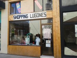 Fachada de tienda "Shopping Lugones" con ropa en el escaparate y carteles en la puerta.