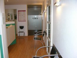 Wartezimmer mit Holzboden, moderner Beleuchtung und mehreren Stühlen an der Wand.