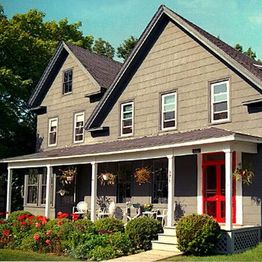 Charming gray house with a red door, porch, and garden full of flowers under a clear sky.