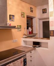 Küche mit gelben Wänden, Herd, weißem Schrank, Wanddekorationen und einem Fenster.