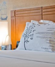 Quarto de hotel com almofada decorativa e mural de árvore na parede ao fundo.