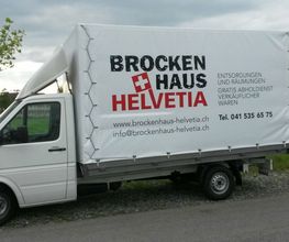 Weißer Lieferwagen mit "Brockenhaus Helvetia"-Werbung geparkt auf einer Straße.