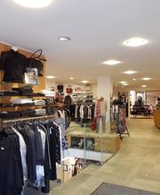 Kleidungsgeschäft Innenansicht mit Kleiderständern, einer Schaufensterpuppe und einem Schalter.