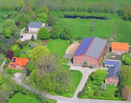 Luftaufnahme eines Bauernhofs mit Gebäuden, Photovoltaikmodulen und grüner Umgebung.