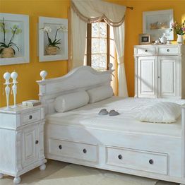 Weißes Schlafzimmer mit gelben Wänden, weißen Möbeln und Orchideen an den Wänden.